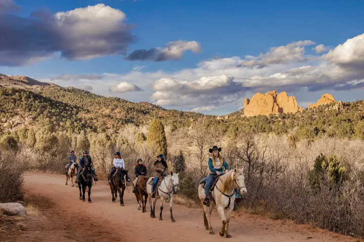 a group of people riding horses on a dirt road